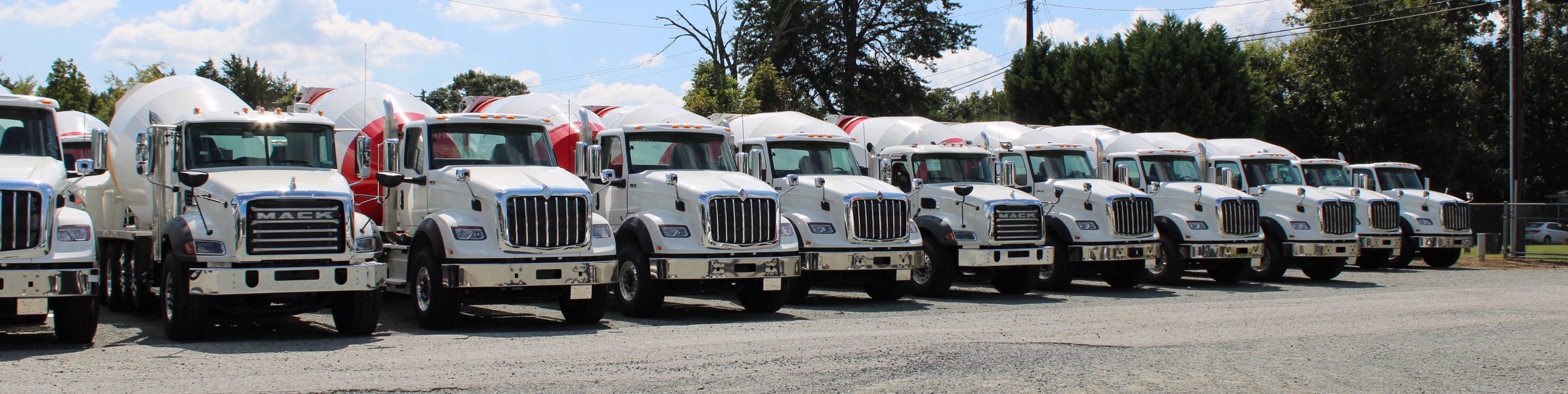 A row of new concrete mixer and dump trucks parked in the Grooms Heavy Truck Sales lot